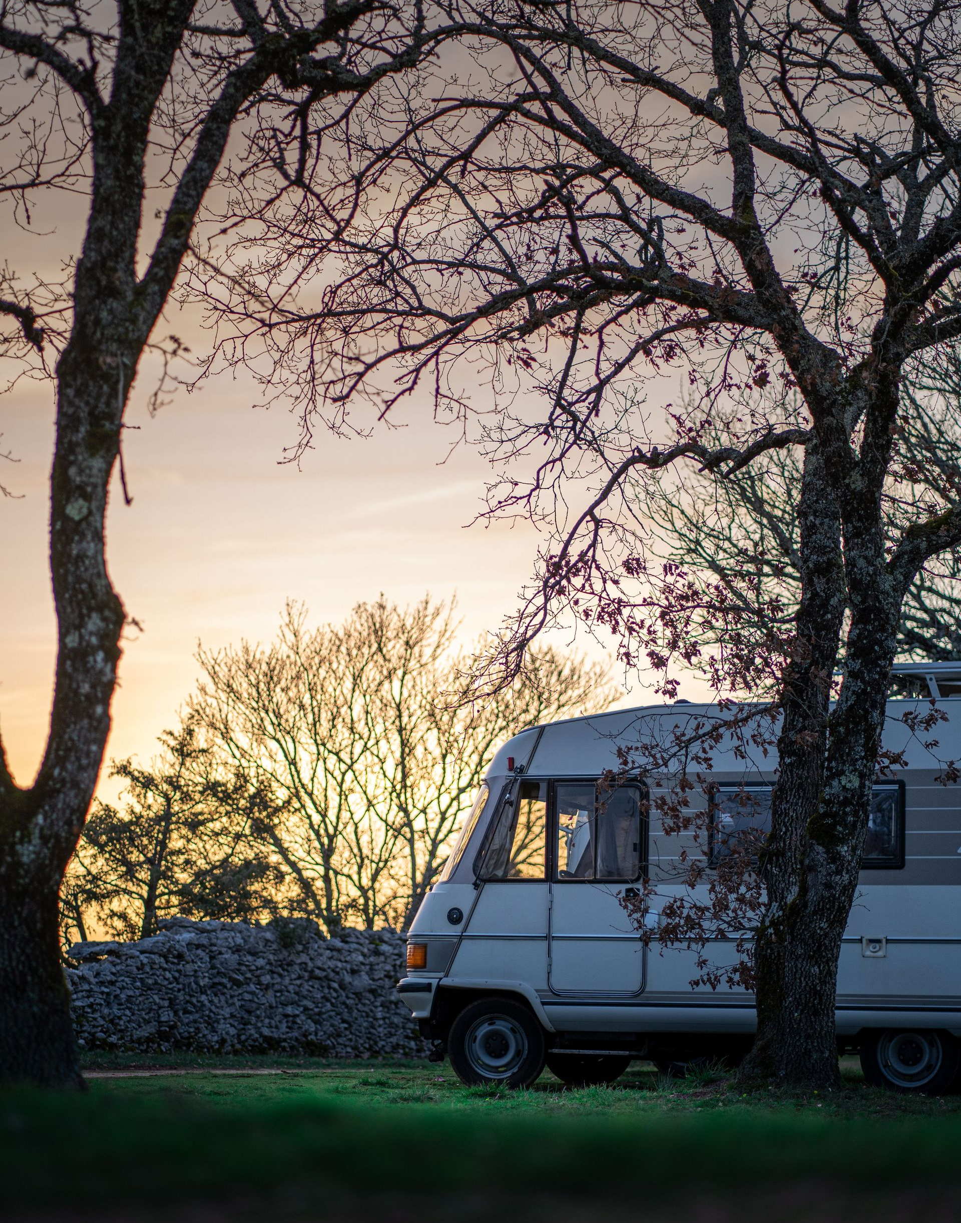 White camper van parked by trees at sunset, with a glowing sky in the background