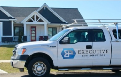 An executive pest solutions truck is parked in front of a house