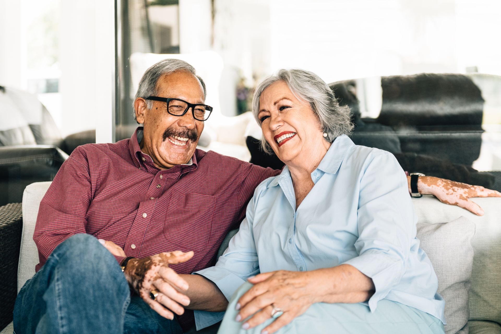Couple laughing together on a couch; man in red shirt, woman in blue, both with henna tattoos.