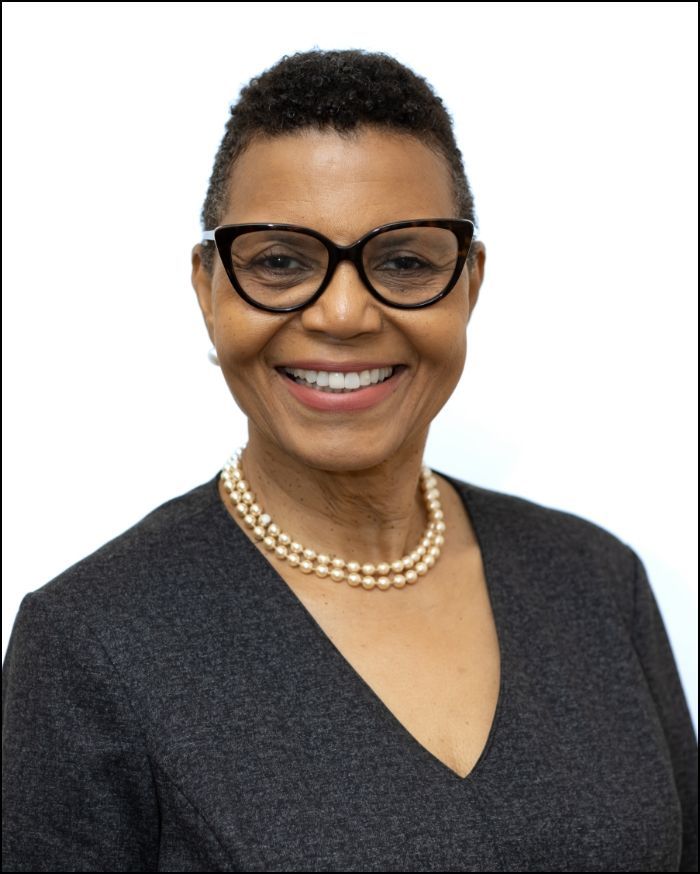 Woman wearing glasses and pearl necklace smiling, against a white background.