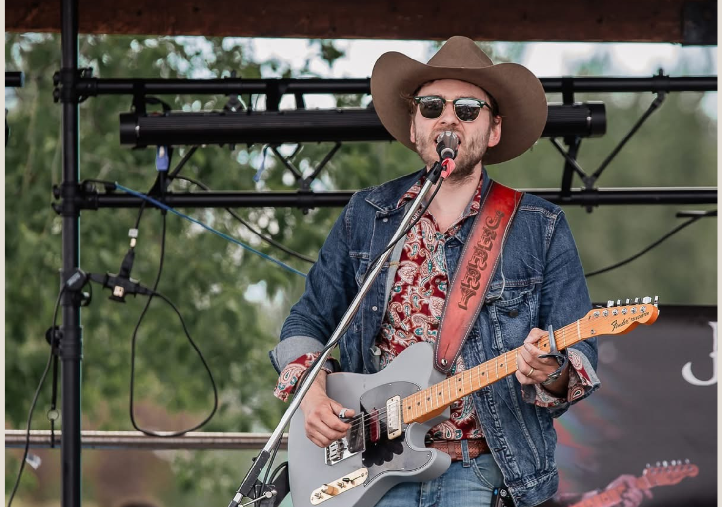 Man in cowboy hat plays guitar on stage, singing into a microphone.