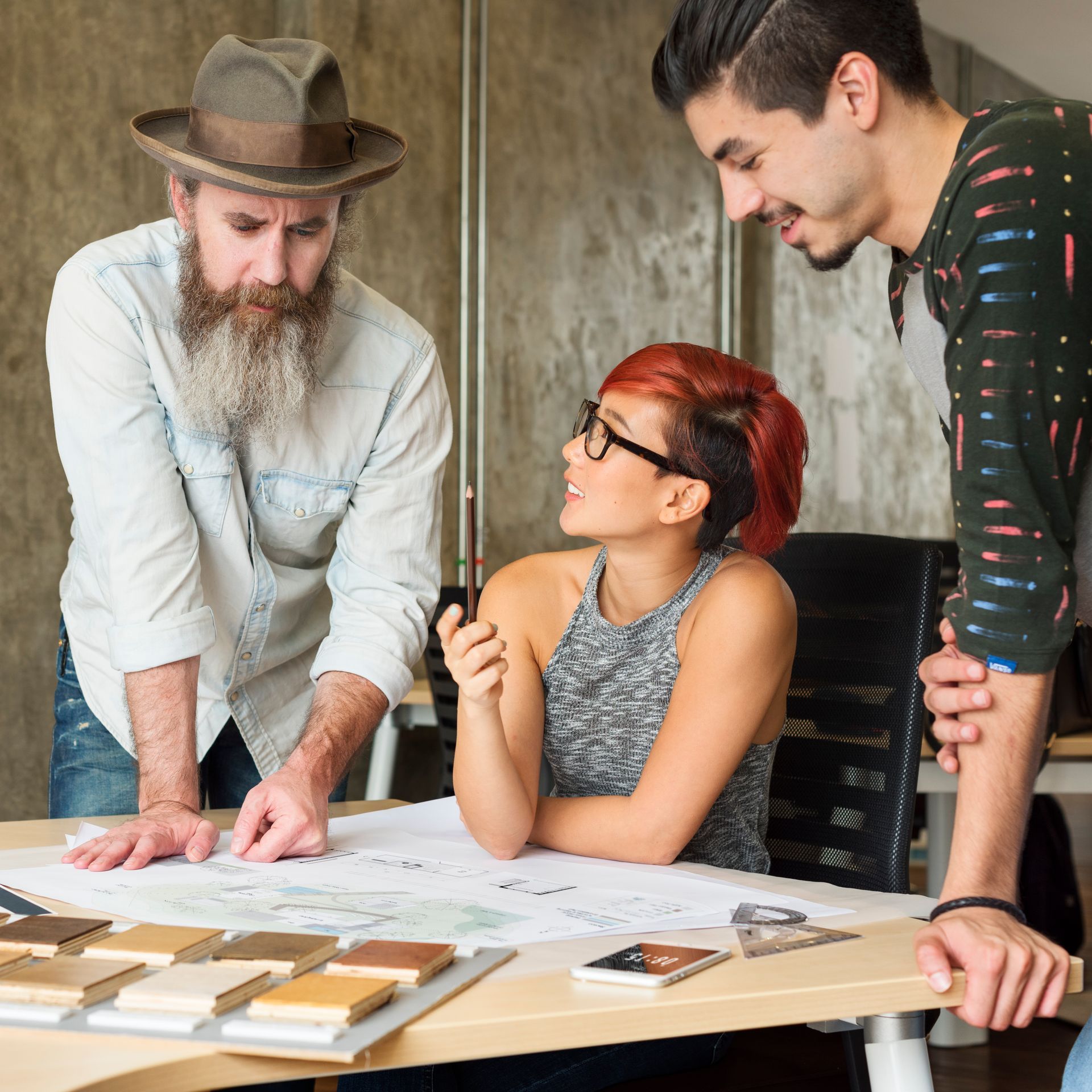 Three people collaborate around a table, examining a blueprint and color samples.