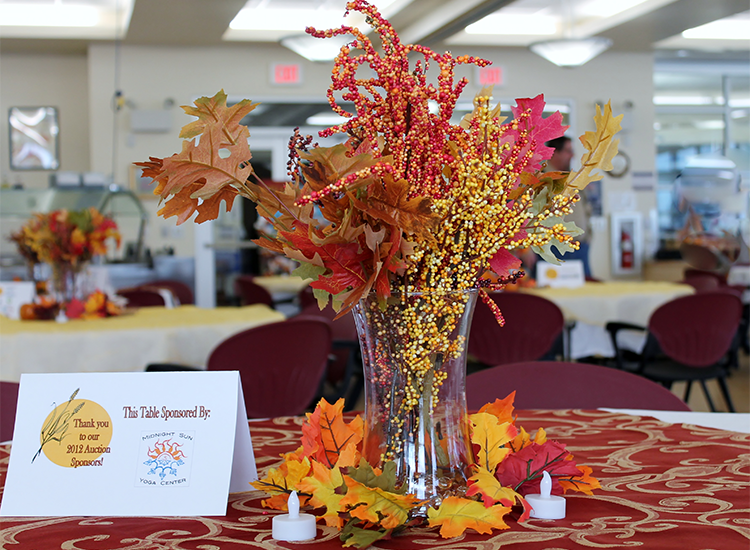 Fall-themed centerpiece with flowers and leaves on a table, flanked by candles and a thank you sign.