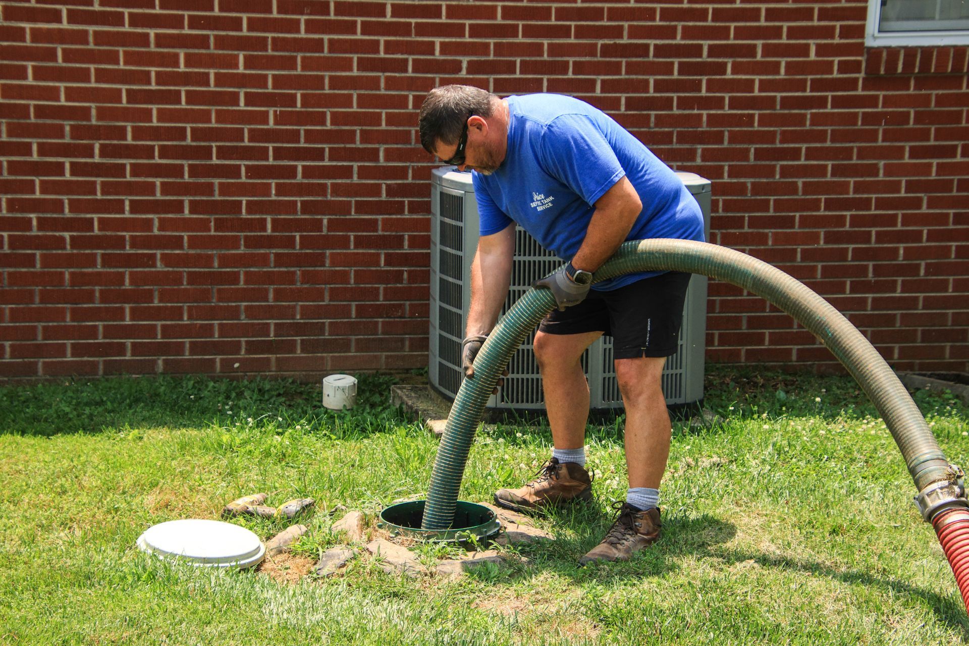 A man in a blue shirt is pumping a hose into a septic tank.