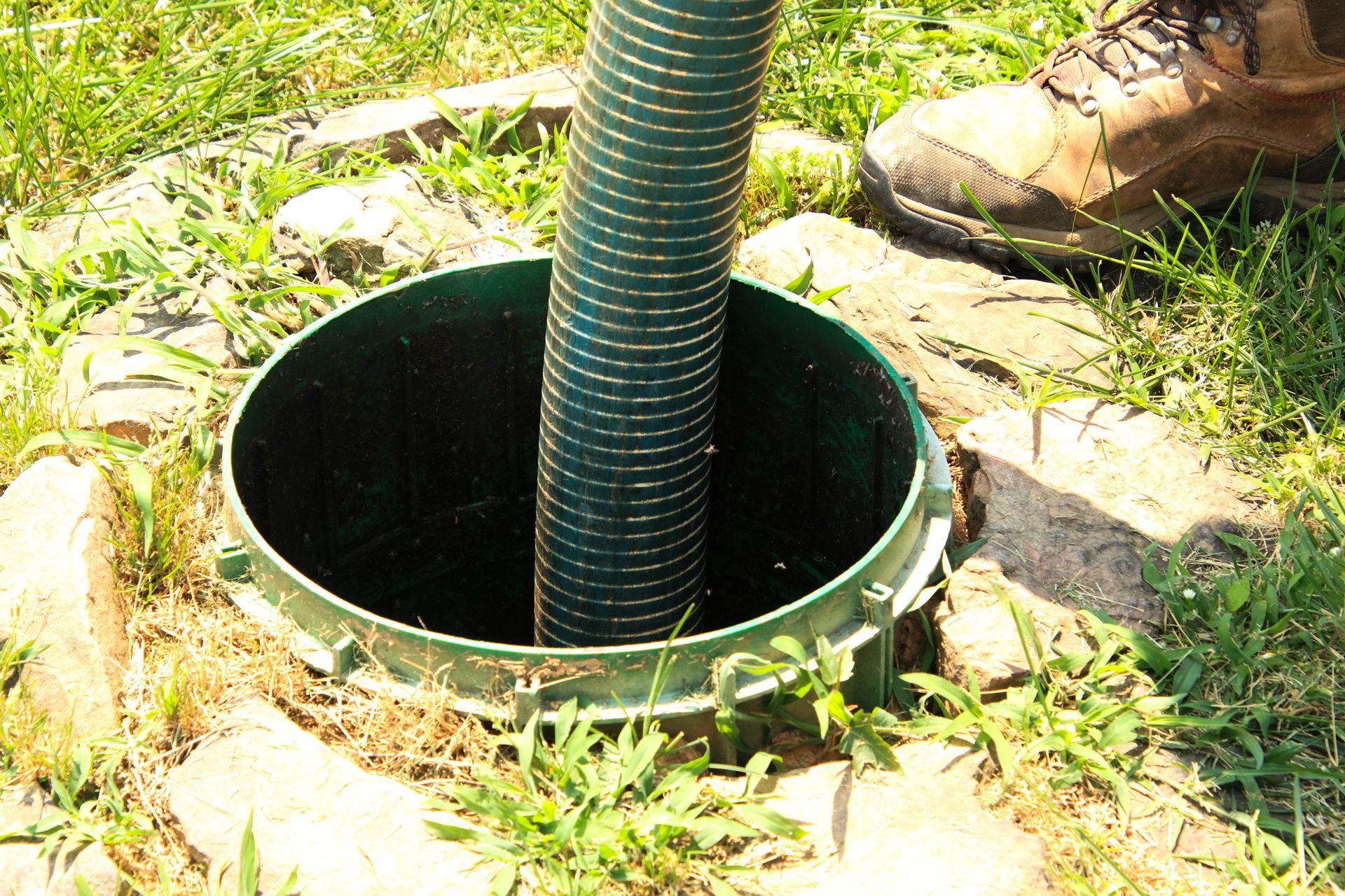 A green hose is coming out of a hole in the ground.