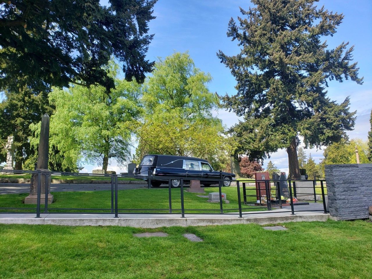 A black van is parked in a cemetery with trees in the background.