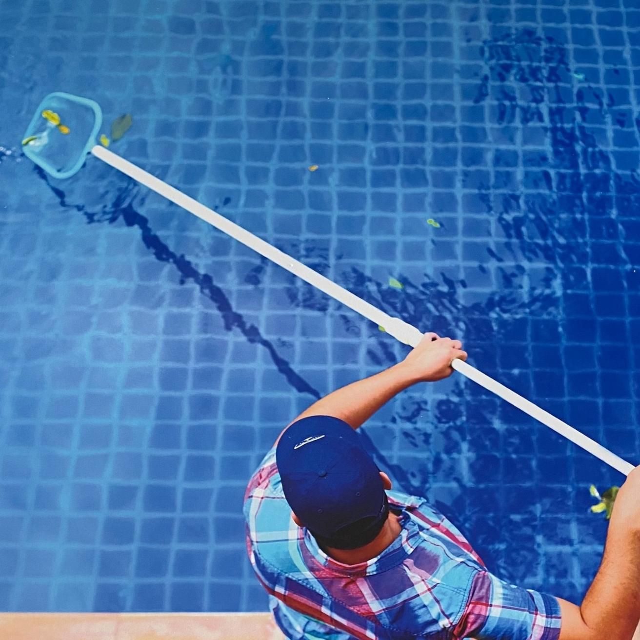 A Man Is Cleaning A Swimming Pool With A Net — Ballina Pool Shop In Ballina, NSW