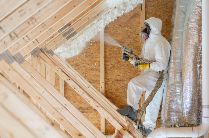 Worker spraying insulation in an attic with exposed wooden framing