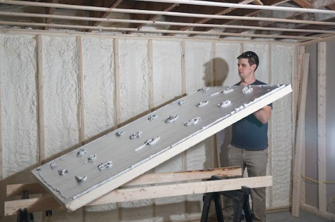 Person in a basement stands beside a large slanted insulated panel mounted on a wooden frame.