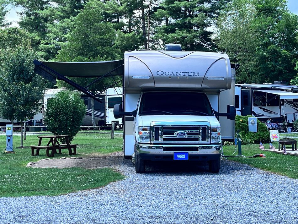 A white rv with a blue license plate is parked in a gravel lot