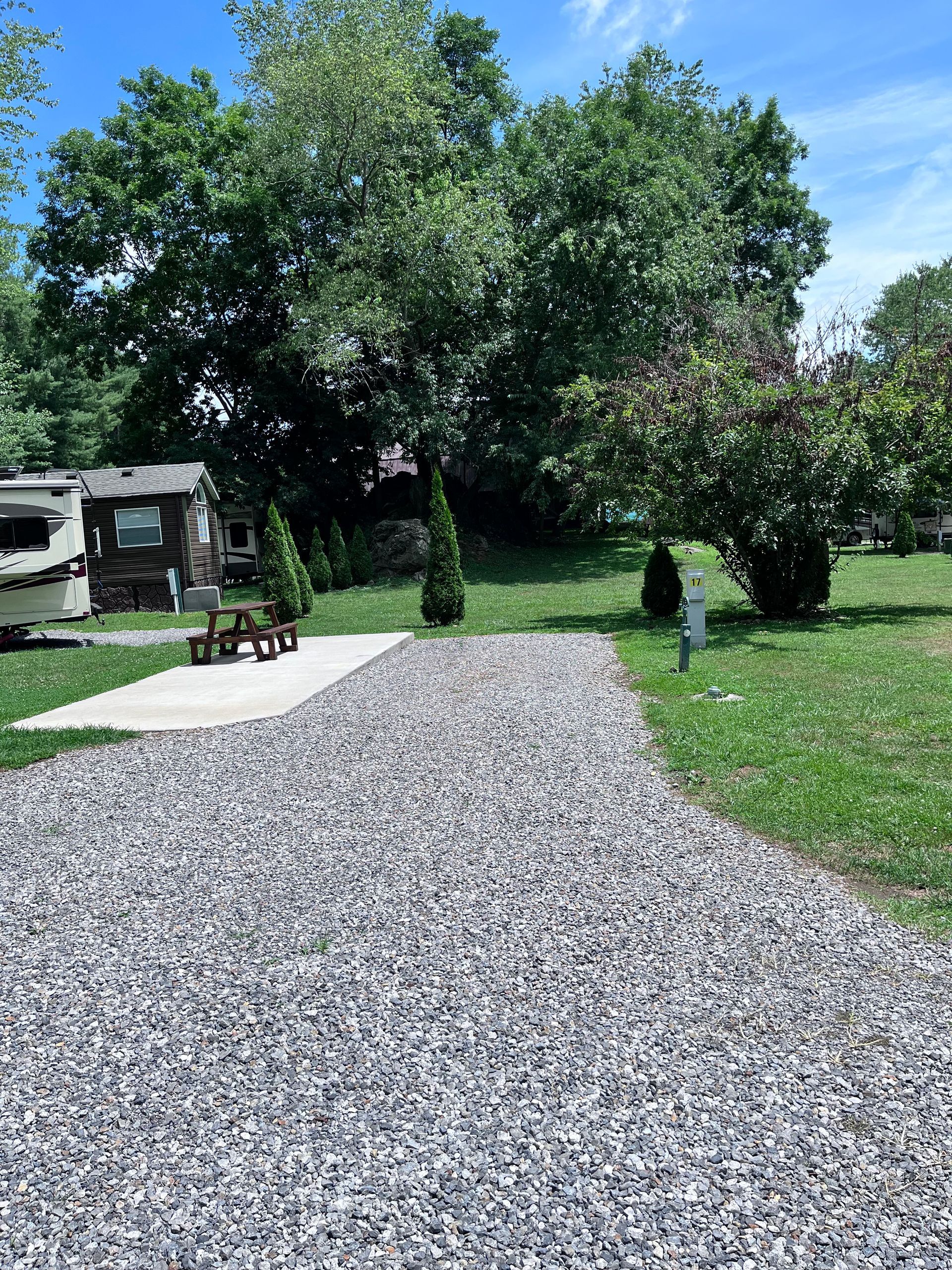 A gravel road leading to a rv parked in the grass.