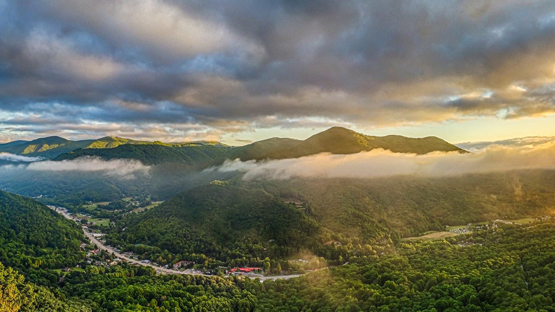 An aerial view of a valley surrounded by mountains and clouds at sunset.