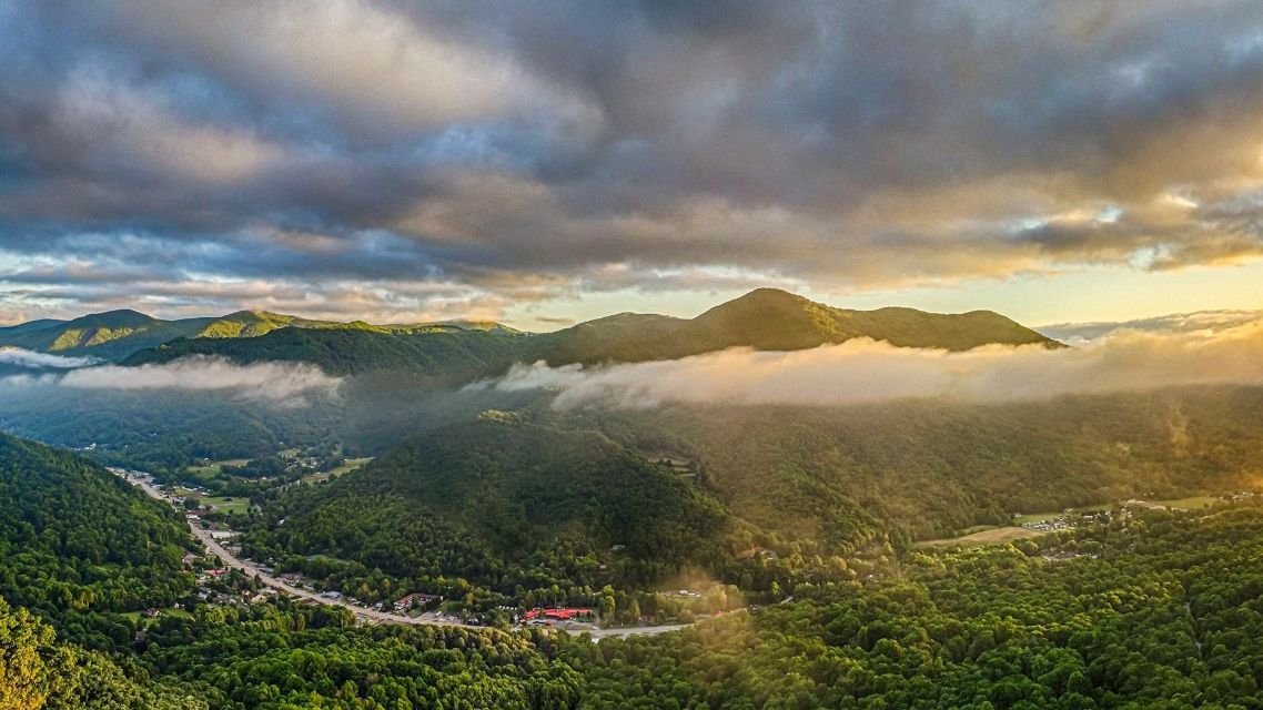 An aerial view of a valley surrounded by mountains and trees at sunset.