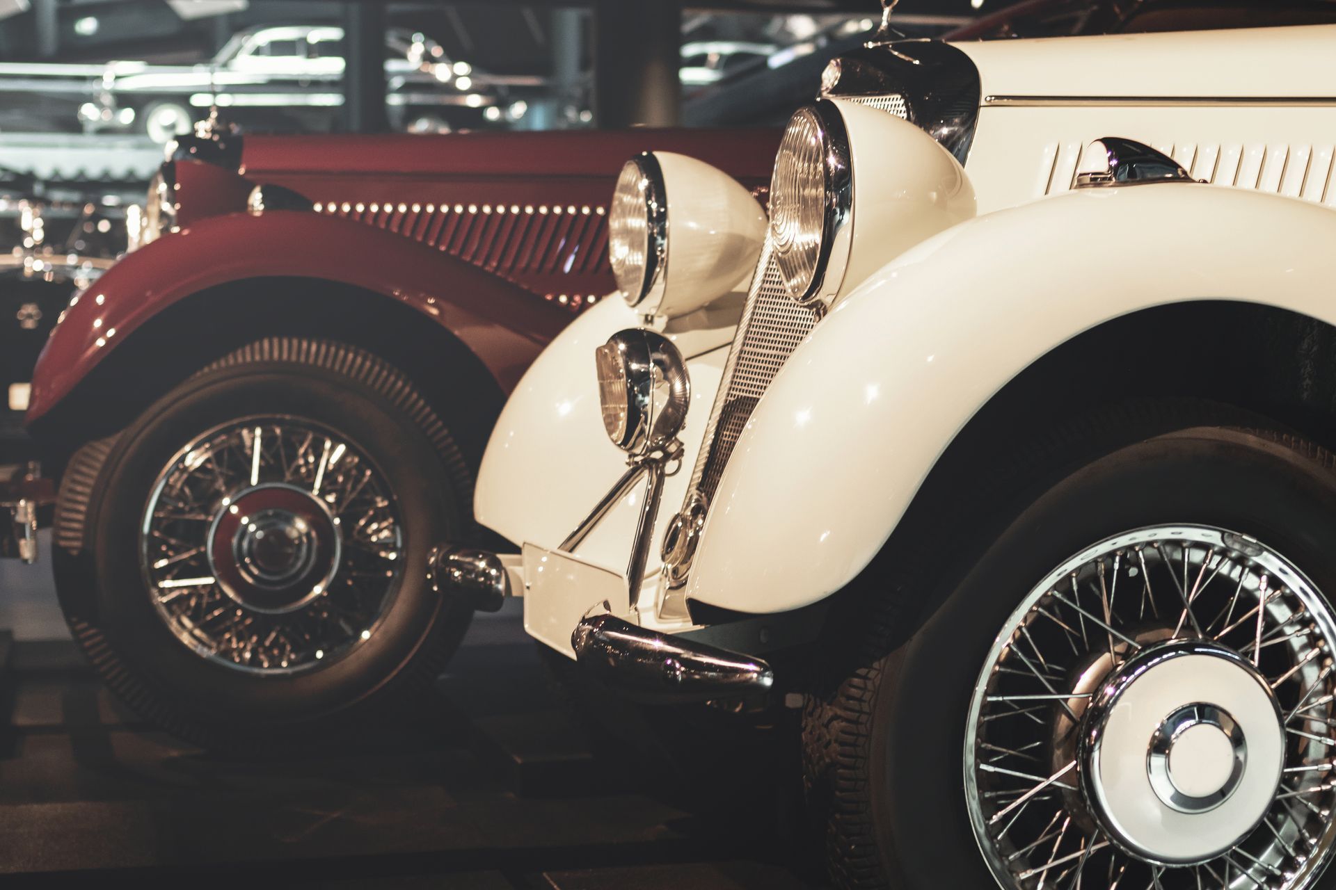 Close-up of a white vintage car parked next to a dark red classic car inside a museum setting.