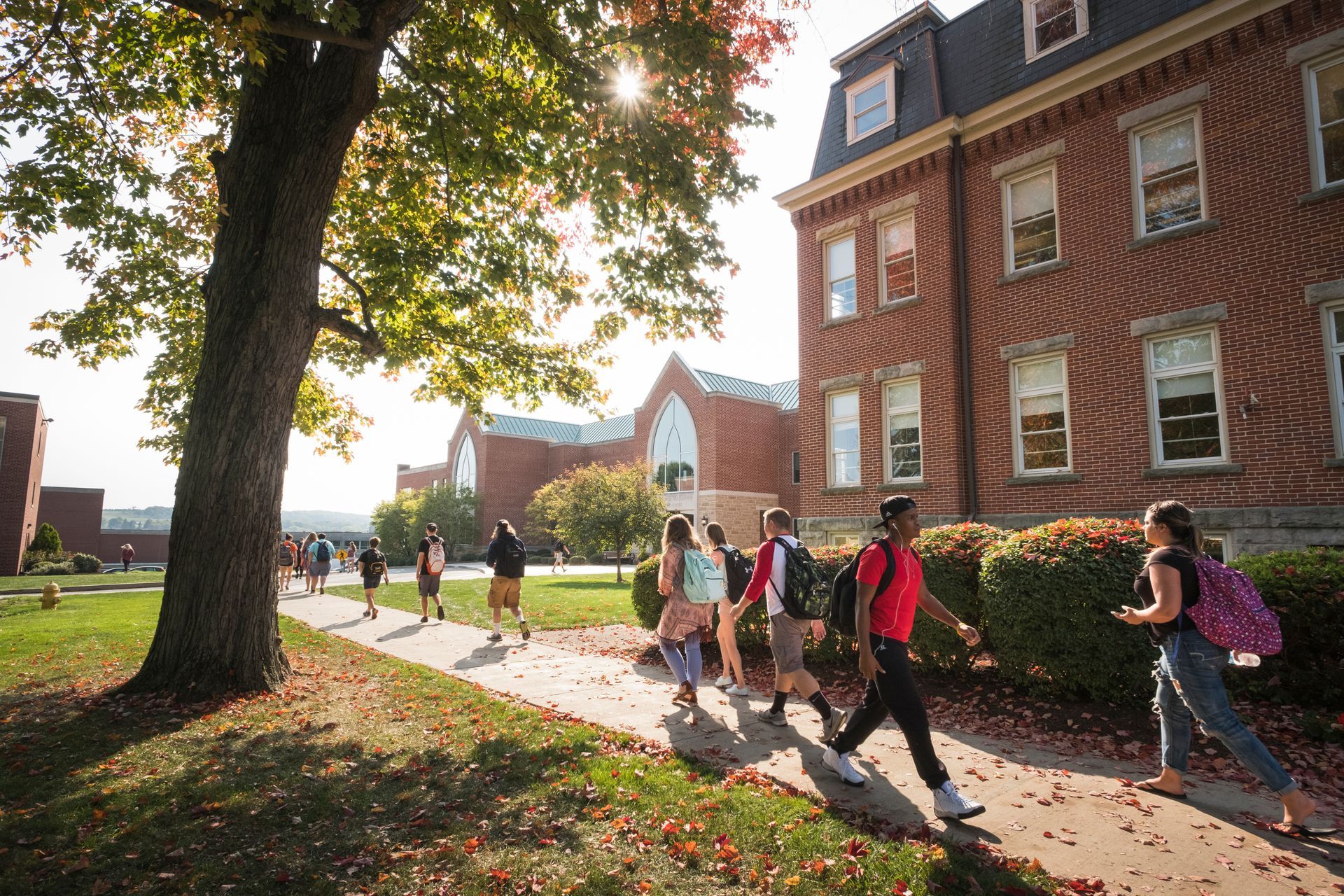 A group of people are walking down a sidewalk in front of a large brick building.