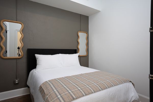 A bedroom with a bed and two mirrors on the wall. Plaid blanket on the bed.