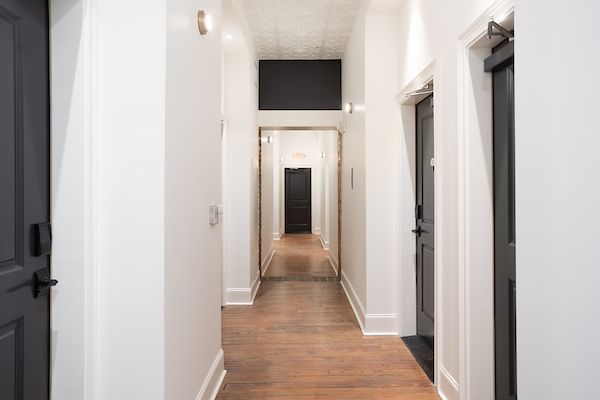 A long hallway with white walls and wooden floors and black doors.