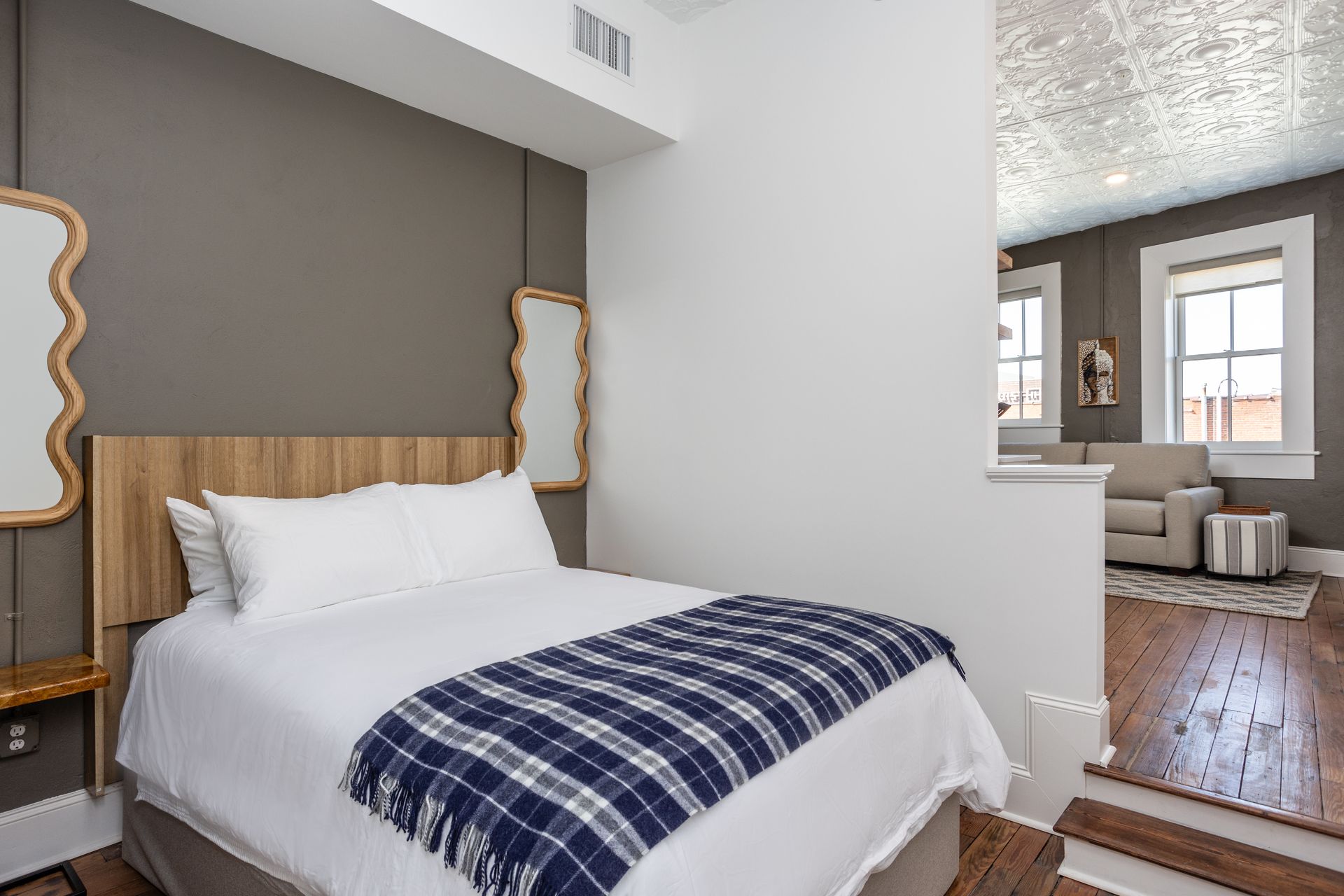 A bedroom with a bed and two mirrors on the wall. Plaid blanket on the bed.