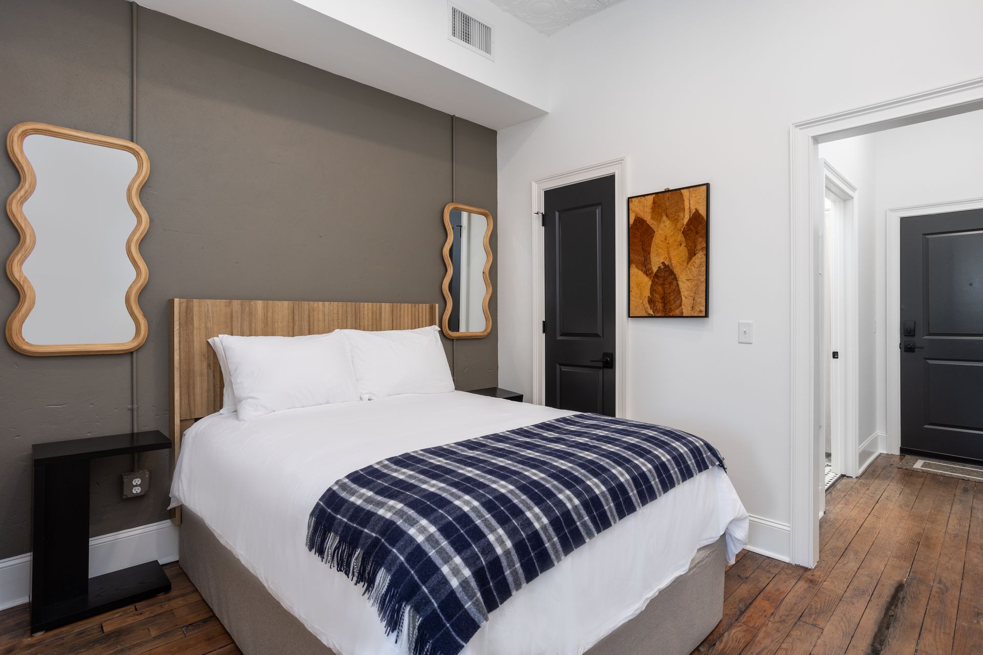 A bedroom with a bed and two mirrors on the wall. Plaid blanket on the bed.