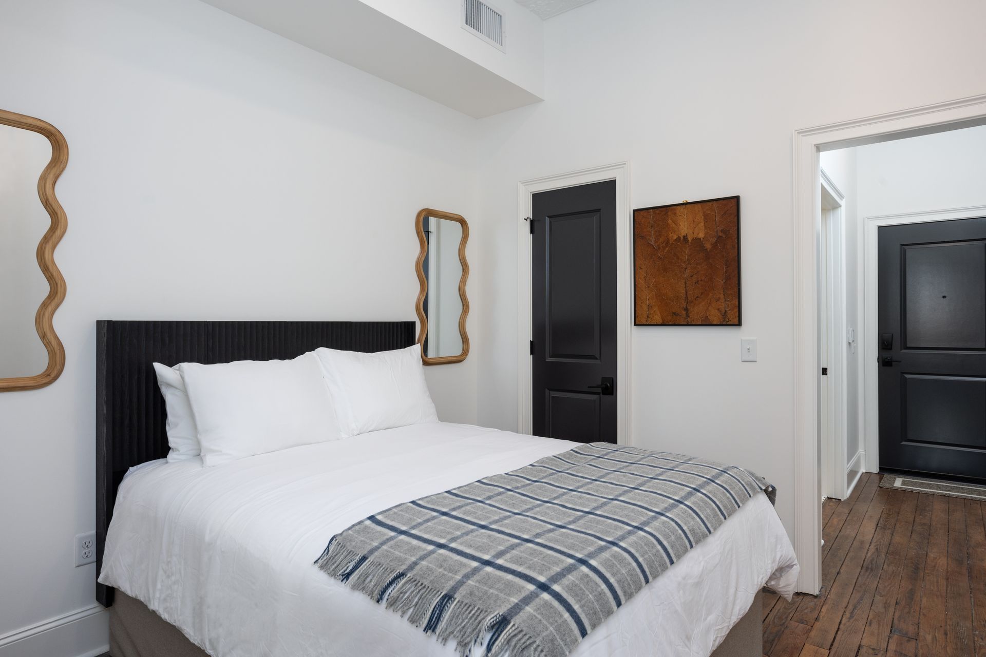 A bedroom with a bed and two mirrors on the wall. Plaid blanket on the bed.