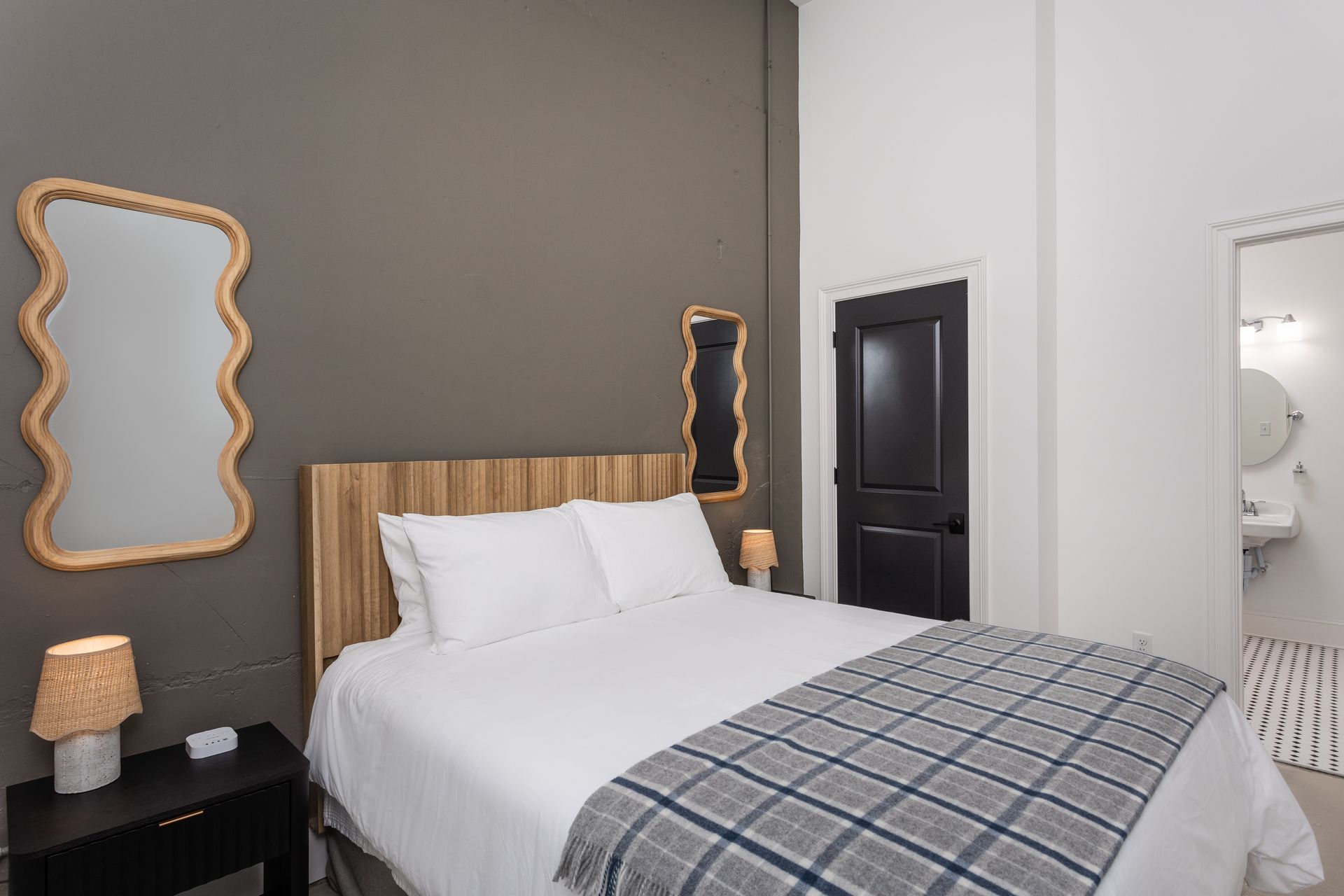 Bedroom with a queen size bed, two wavy mirrors on the wall and a plaid blanket on the bed.