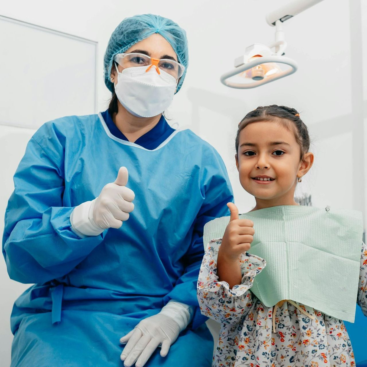 A dentist and a little girl are giving a thumbs up.