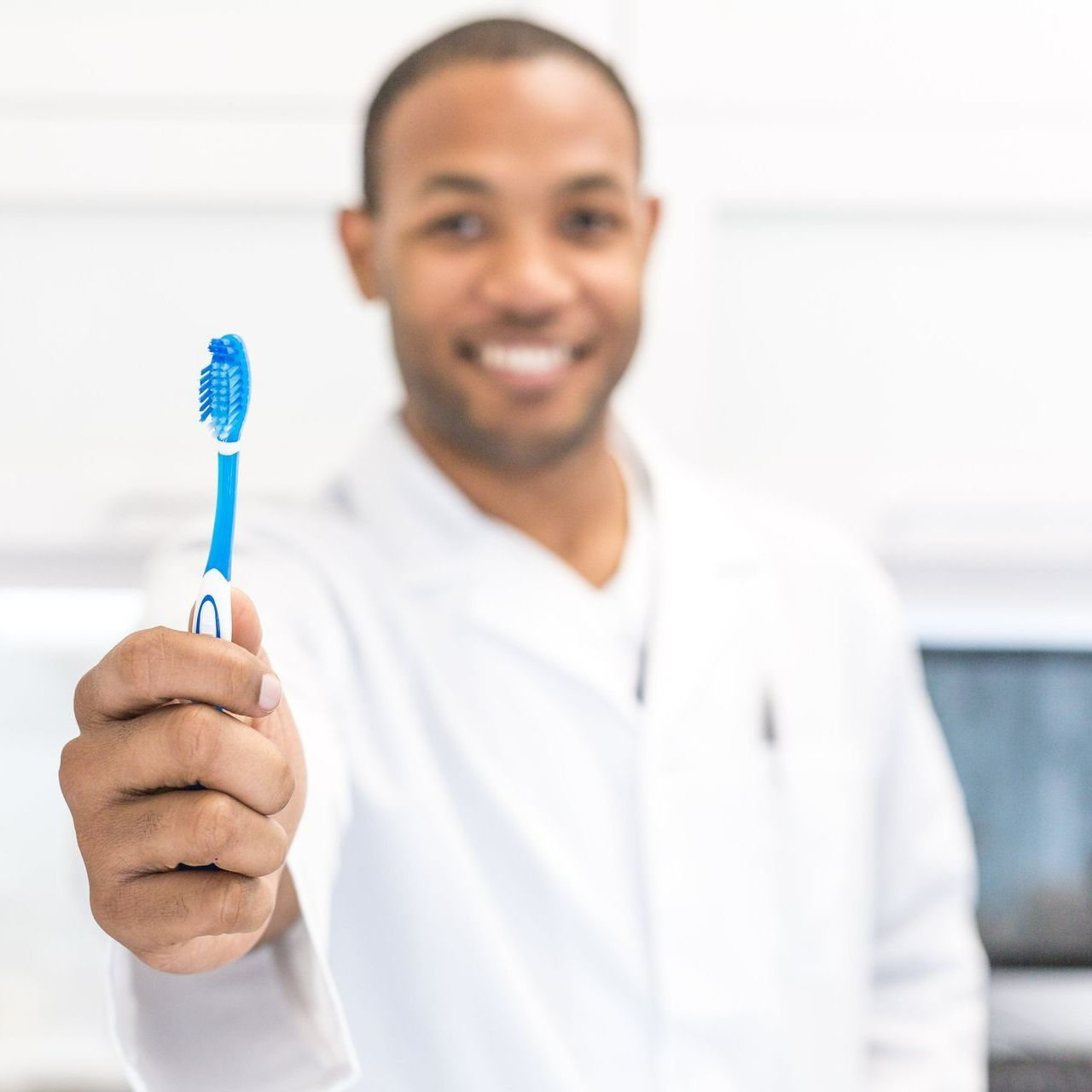 A man in a lab coat is holding a blue toothbrush