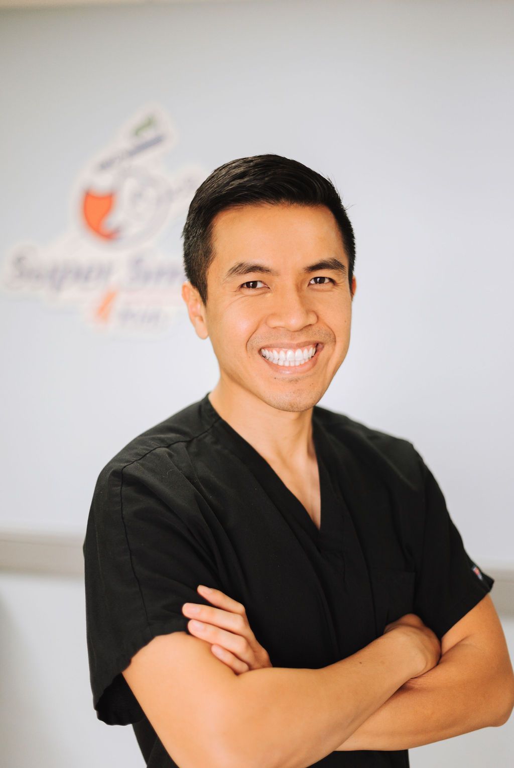 A man in a black scrub top is smiling with his arms crossed.