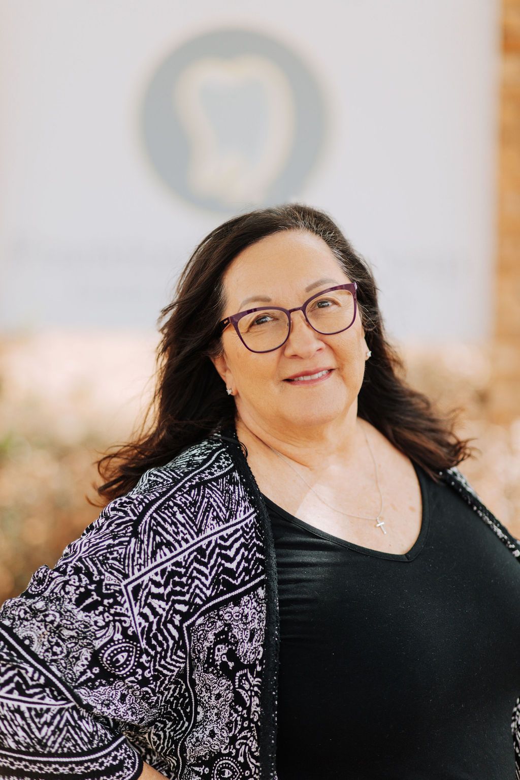 A woman wearing glasses and a black shirt is standing in front of a wall.