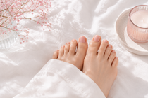Bare feet on a white bed beside a pink candle and dried flowers