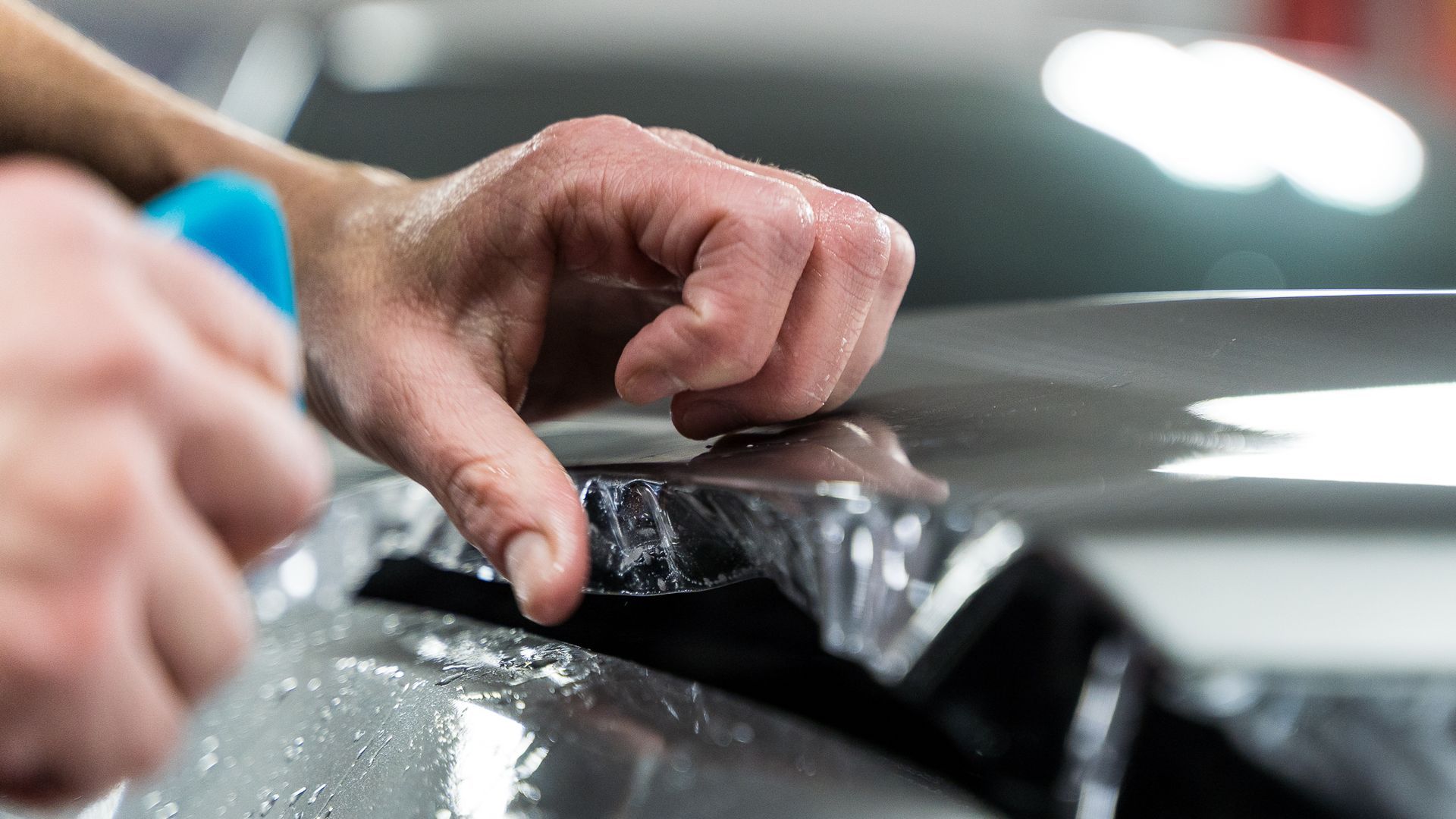 Satin Paint Protection Film - A person is applying a clear plastic covering to a car