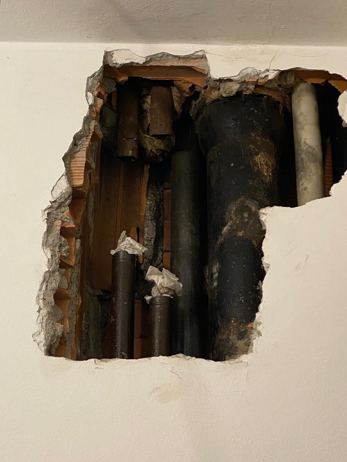 Un buco nel muro da cui escono dei tubi.