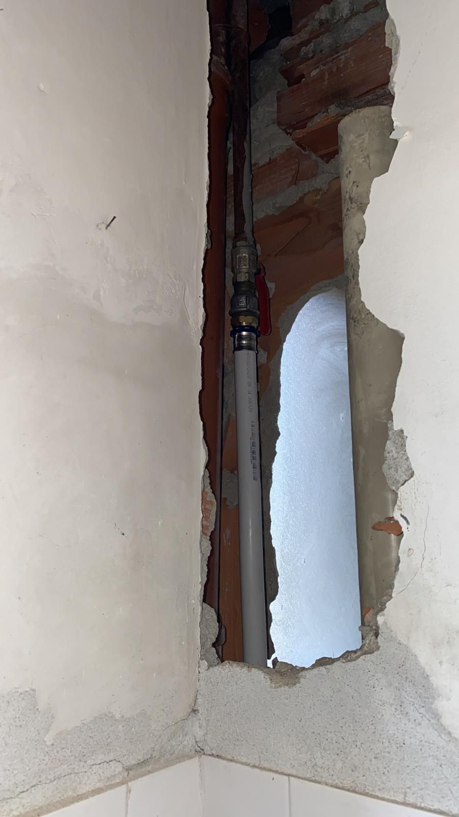 Un buco nel muro da cui esce un tubo.