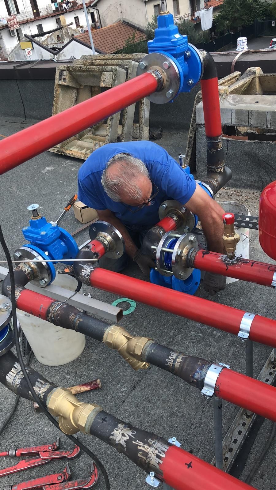 Un uomo con una camicia blu sta lavorando su tubi rossi.