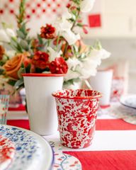 A red and white cup is sitting on a table next to a vase of flowers.