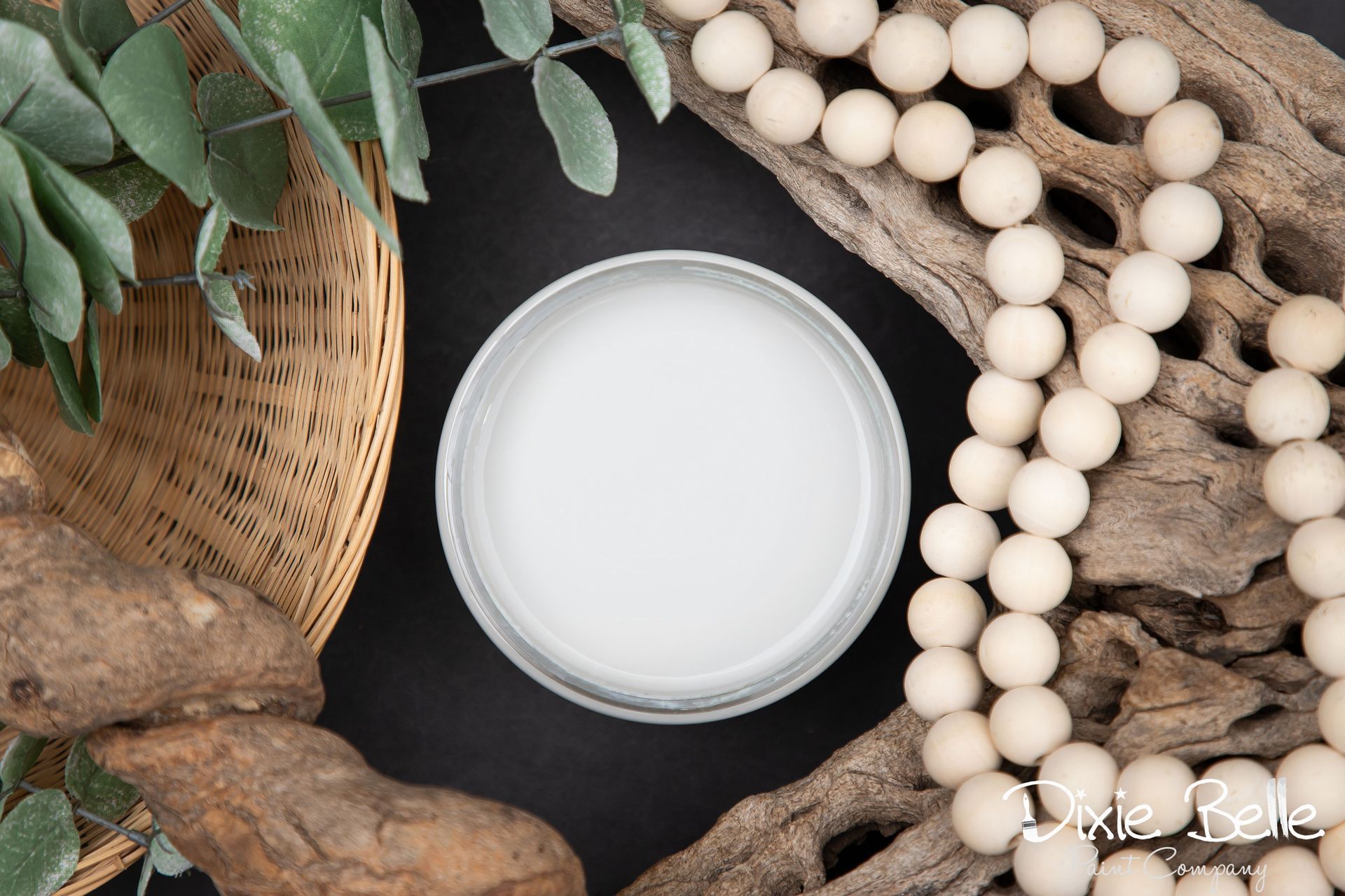 A bowl of white paint next to a necklace of white beads.