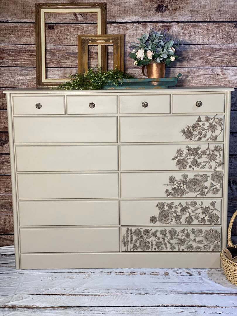 A white dresser with a floral design on it is sitting on a wooden table.