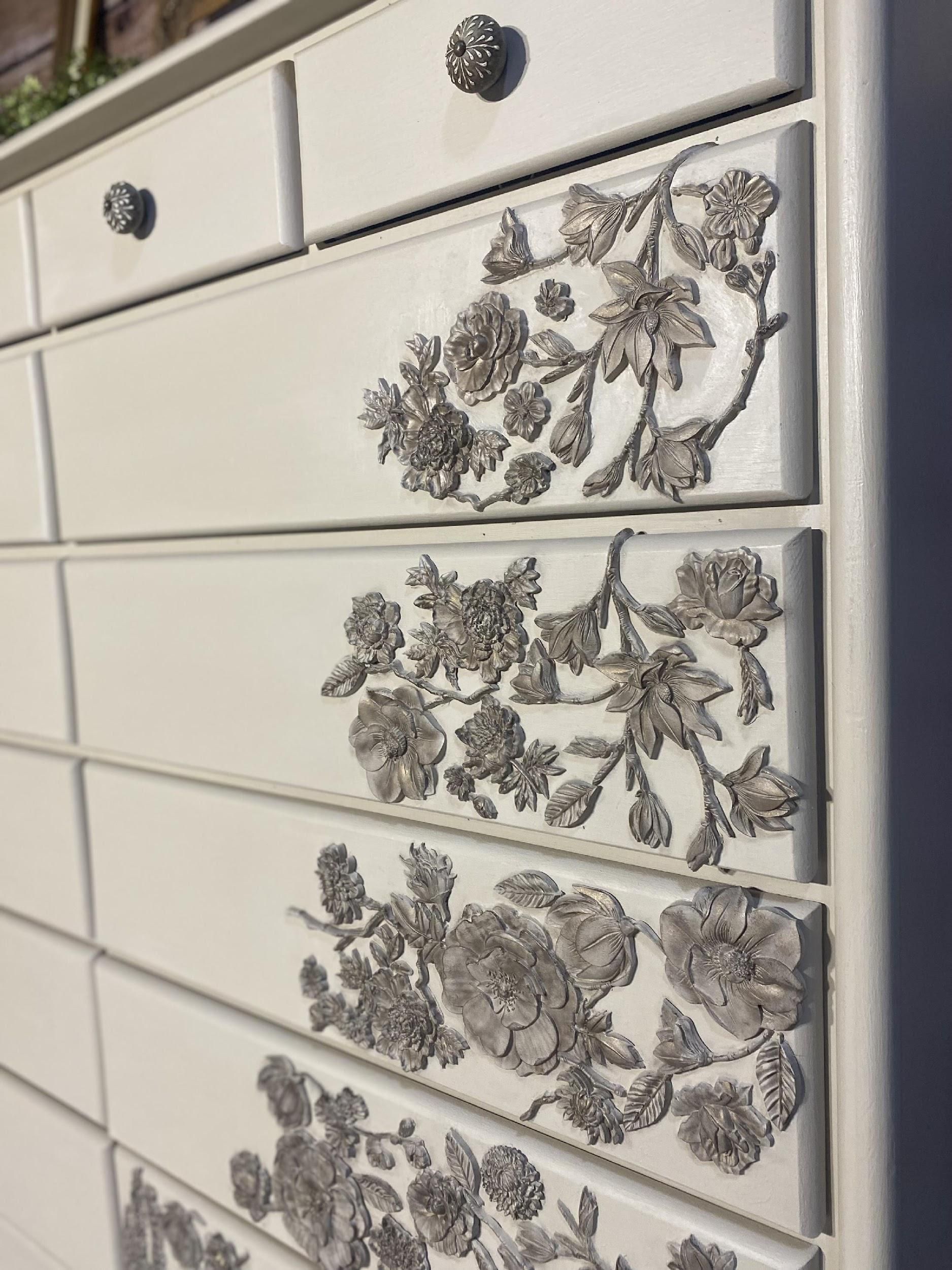 A close up of a white dresser with flowers on the drawers.