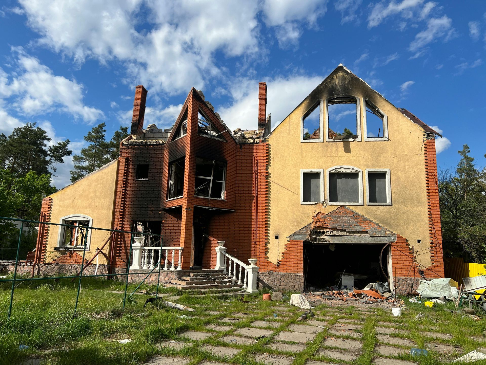 Abandoned brick house with broken windows and overgrown yard under a blue sky
