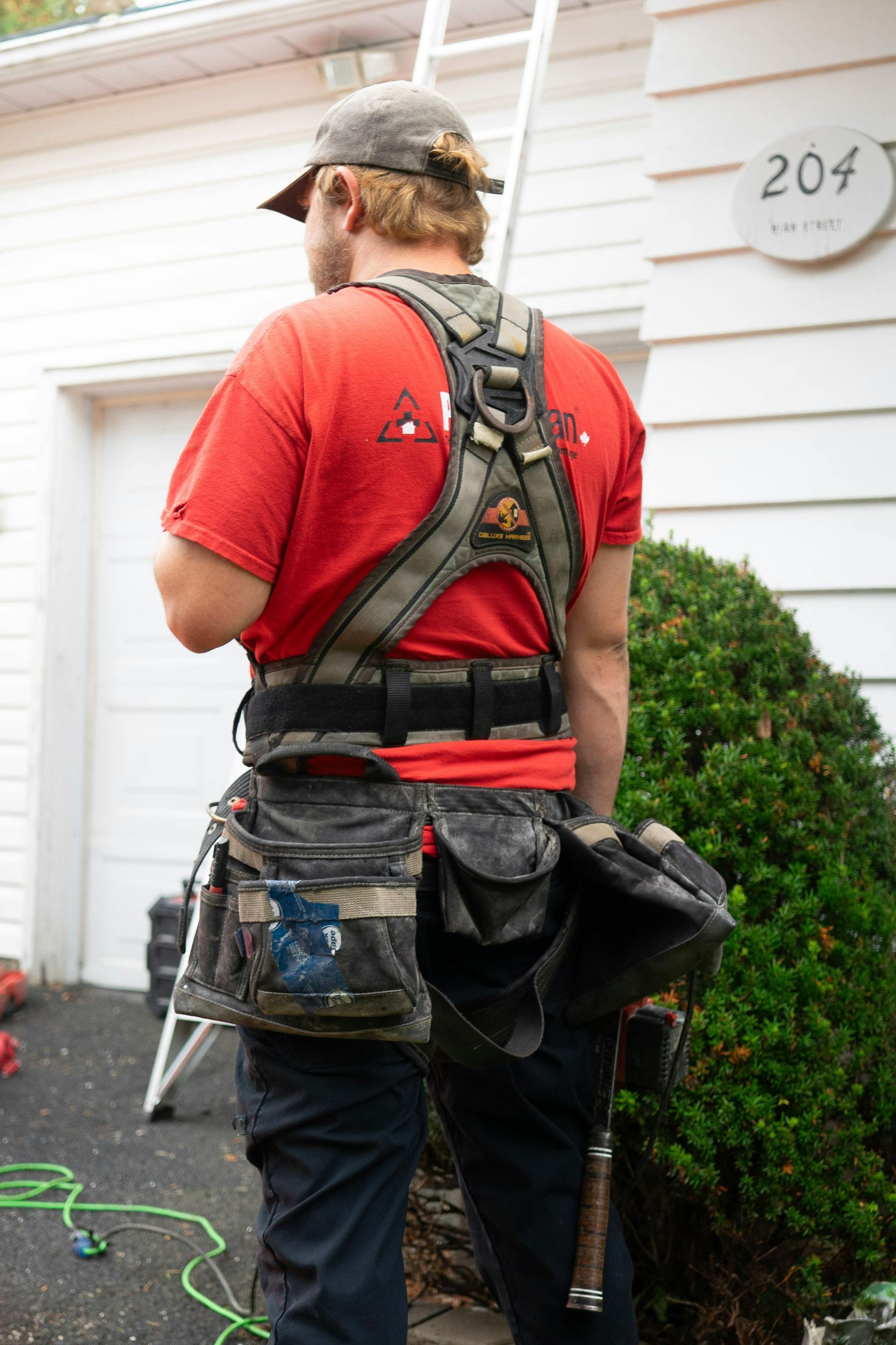 Utility worker in red shirt and tool belt working beside a house and hedge
