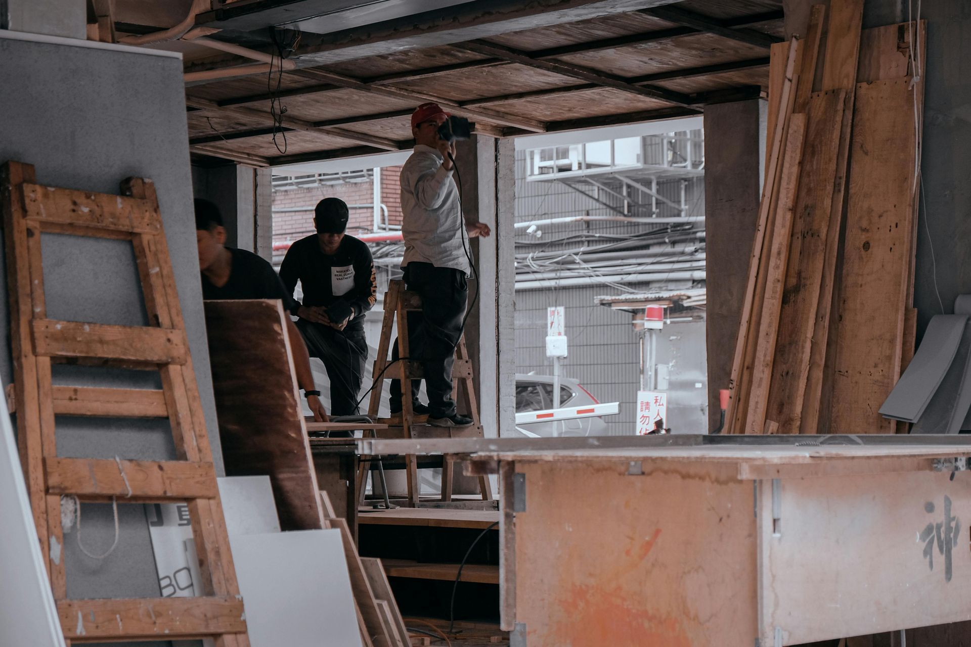 Workers inside a partially built room with wood framing, standing on a platform amid construction materials
