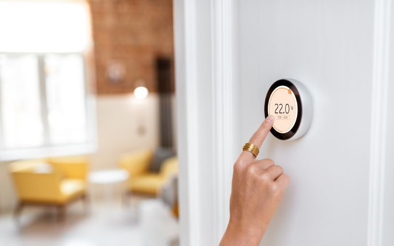 A person is pressing a button on a thermostat in a living room.