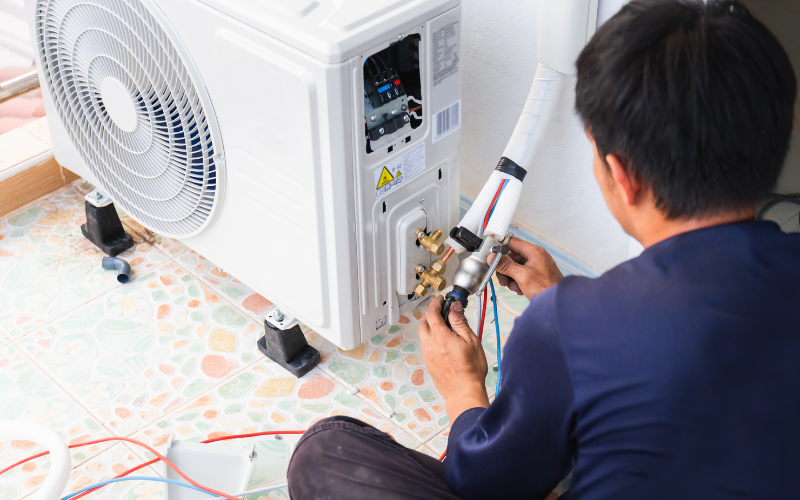 A man is sitting on the floor fixing an air conditioner.