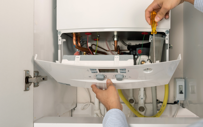 A person is fixing a boiler with a screwdriver.