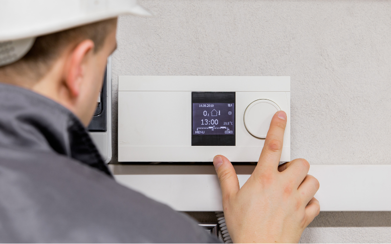A man is adjusting a thermostat on a wall.