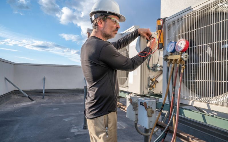 A man is working on an air conditioner on the roof of a building.