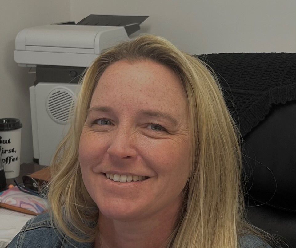 A woman is smiling while sitting in front of a printer