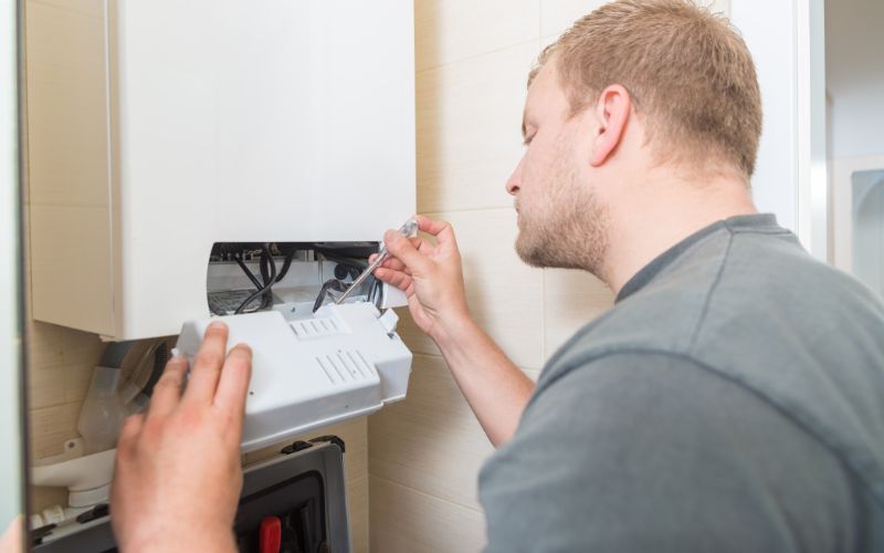 A man is fixing a boiler with a screwdriver.