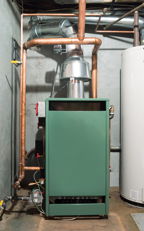A green boiler is sitting in a basement next to a white water heater.