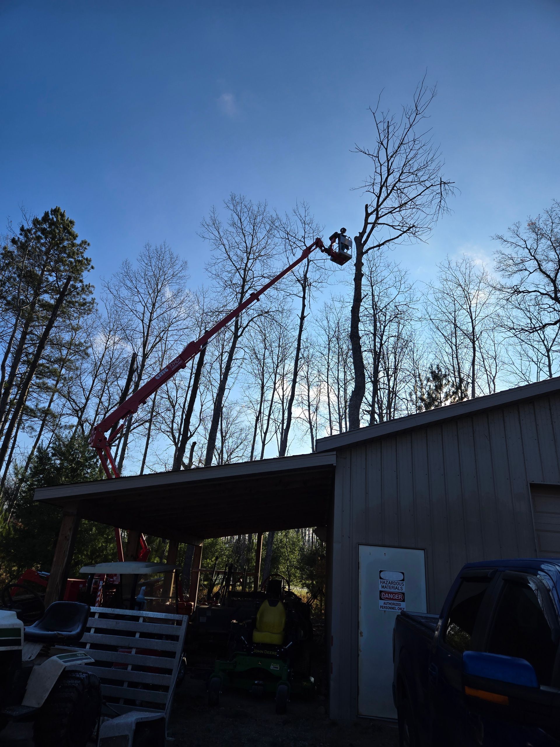 A man is cutting a tree with a crane in front of a garage.